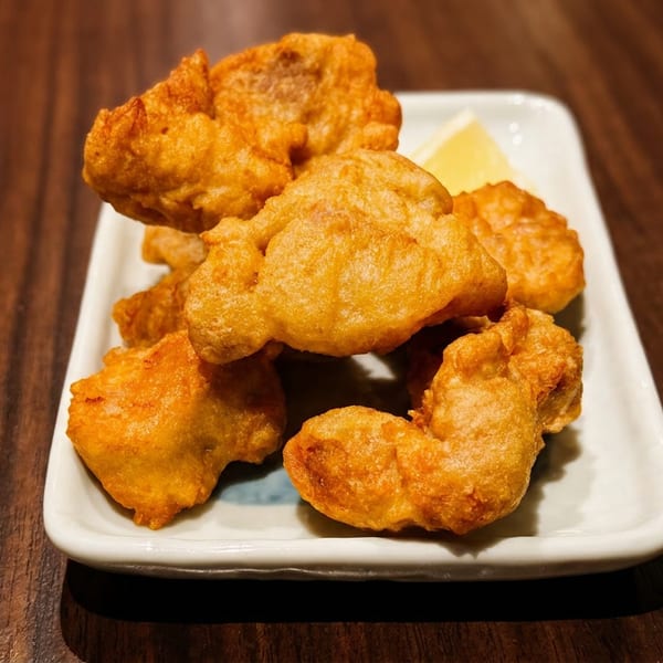 Plate of golden fried chicken karaage with a lemon wedge on a dark wooden table.