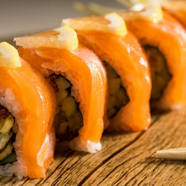 Salmon sushi rolls topped with lemon slices, arranged on a wooden board with chopsticks.