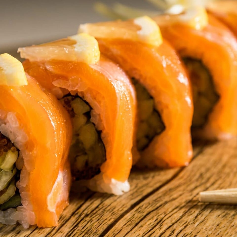 Salmon sushi rolls topped with lemon slices, arranged on a wooden board with chopsticks.
