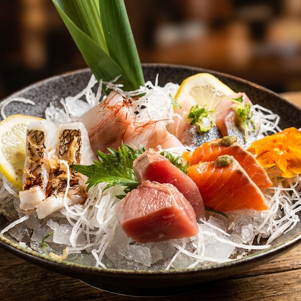 Assorted fresh sashimi platter with salmon, tuna, and white fish, served on ice with lemon and flowers.