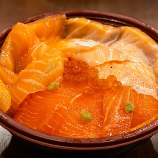 A bowl of vibrant orange salmon sashimi, glistening roe, and green wasabi dots.