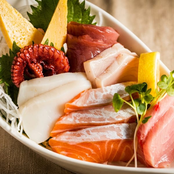 Colorful sashimi platter with salmon, tuna, octopus, squid, tamagoyaki, and fresh garnishes.